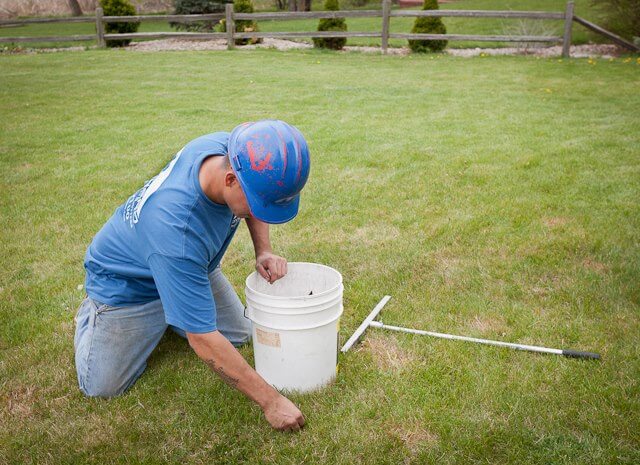 Roofing contractor picking up nails from the grass after new roof installation.