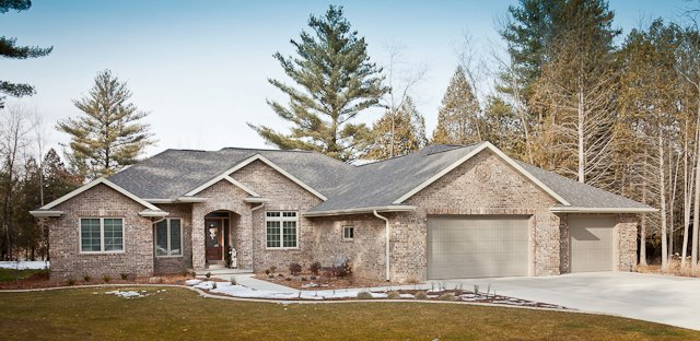 Large stone home surrounded by trees with new roof shingles from Overhead Solutions in Green Bay.